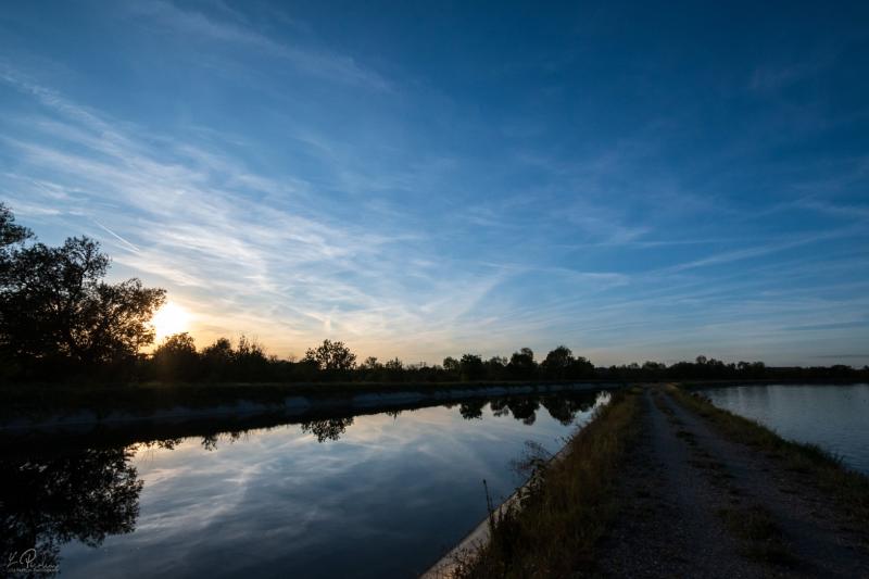 Deep blue sky taken at sunset with some yellow light coming from the horizon. Clouds are reflected on the calm water of the river