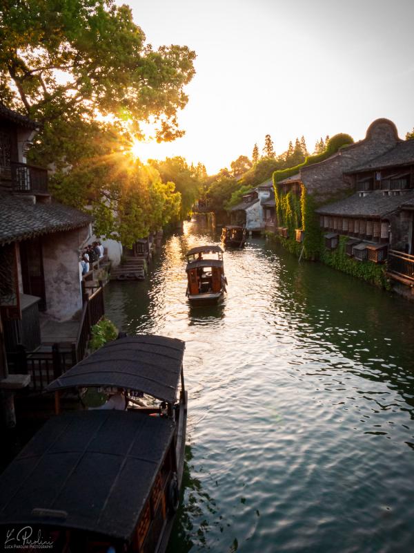 Sunset over a canal in Wuzhen with traditional boats floating on the river and houses on the side
