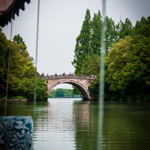 Water reflection of the West Lake in a sunny summer day with tree reflecting on the water and an old bridge in the background