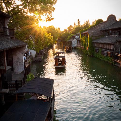 Sunset over a canal in Wuzhen with traditional boats floating on the river and houses on the side